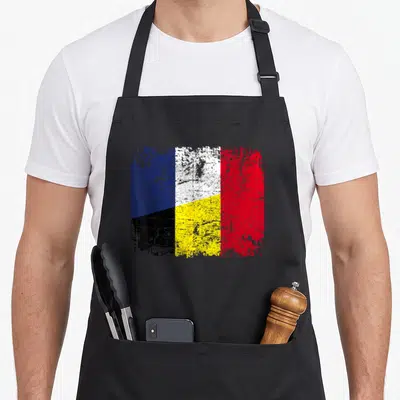 Tablier de cuisine noir avec un drapeau combinant les couleurs belges et françaises dans un style délavé et texturé.