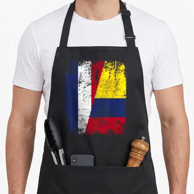 Tablier de cuisine noir avec un drapeau stylisé combinant les couleurs bleue, blanche, rouge et jaune des drapeaux français et colombien dans un effet délavé.