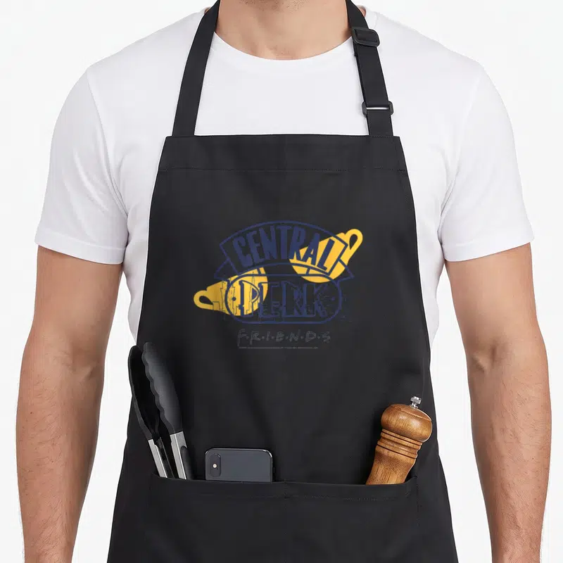 Tablier de cuisine noir avec logo Central Perk Friends en bleu et jaune sur fond gris uni.
