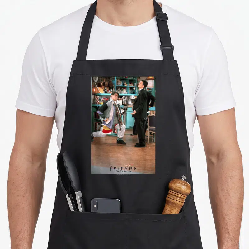 Tablier de cuisine noir avec une scène de deux personnages dans un décor de café bleu turquoise et le logoFriends en bas.