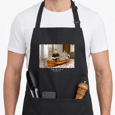 Tablier de cuisine noir avec deux hommes dans une barque en bois à l'intérieur d'un appartement, texteFriends en bas.