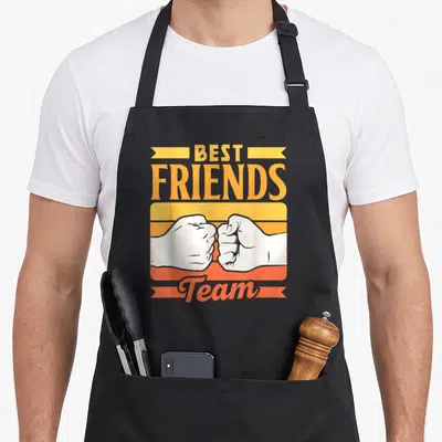 Tablier de cuisine noir avec Best Friends Team et deux poings s'entrechoquant sur fond rétro orange et jaune.