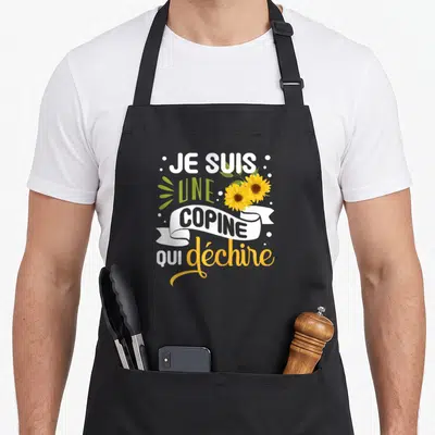 Tablier de cuisine noir avec inscription Je Suis Une Copine Qui Déchire et deux tournesols jaunes.