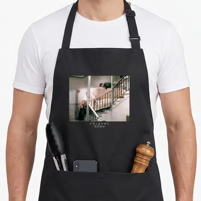 Tablier de cuisine noir avec une scène de staircase et deux personnages assis ou allongés sur un meuble.