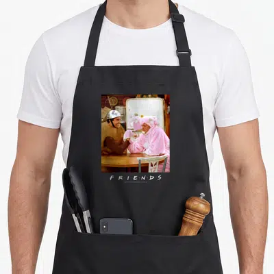 Tablier de cuisine noir avec Ross en casque et Chandler en costume de lapin effectuant un bras de fer comique.