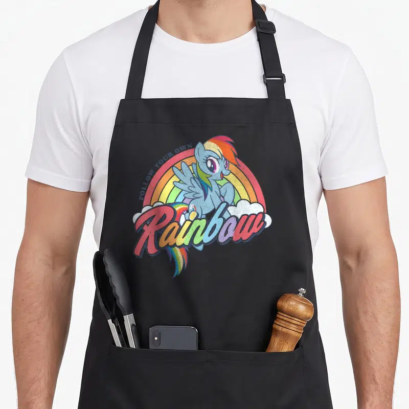 Tablier de cuisine noir avec illustration d'un poney bleu aux cheveux multicolores devant un arc-en-ciel et des nuages blancs.