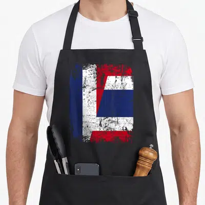 Tablier de cuisine noir avec un motif graphique fusionnant les drapeaux français et thaïlandais dans un style délavé.