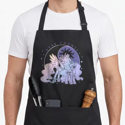 Tablier de cuisine noir avec illustration de deux licornes pastel et l'inscription Stay Cosmic au-dessus d'un motif céleste.