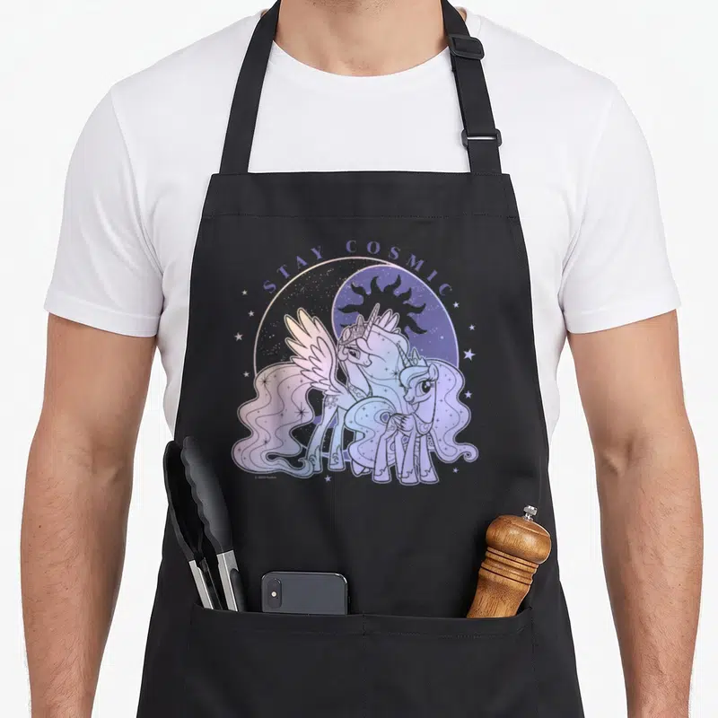 Tablier de cuisine noir avec illustration de deux licornes pastel et l'inscription Stay Cosmic au-dessus d'un motif céleste.