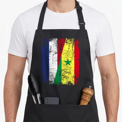 Tablier de cuisine noir avec le drapeau de l'amitié mêlant les motifs français et sénégalais en texture usée.