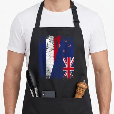 Tablier de cuisine noir avec un drapeau combinant la Nouvelle-Zélande et la France en style vintage.