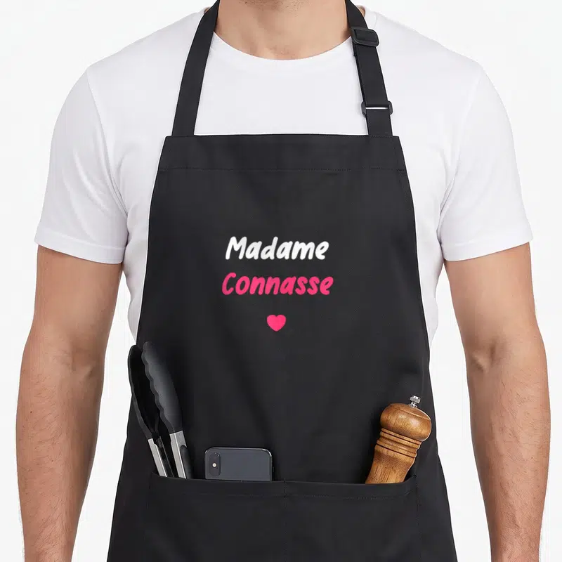 Tablier de cuisine noir avec l'inscription Madame Connasse et un cœur rose vif au centre.