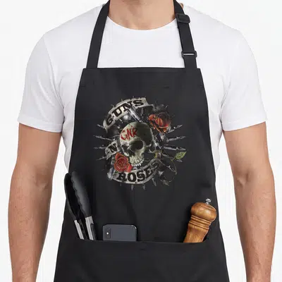Tablier de cuisine noir avec un crâne floral entouré de balles, roses rouges et inscriptions GUNS N ROSES en style tattoo.