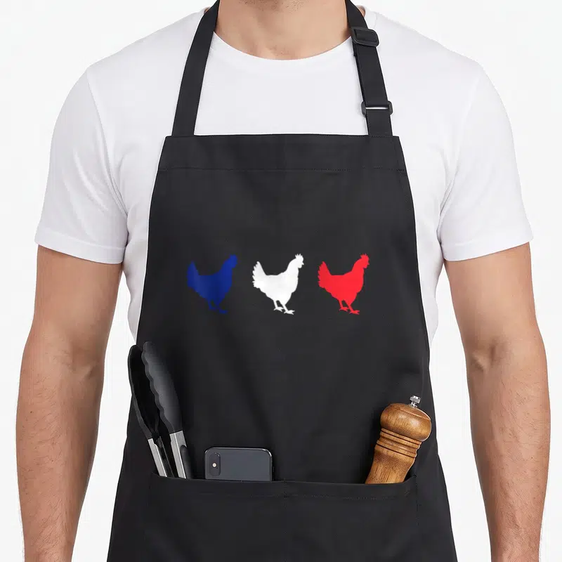 Tablier de cuisine noir avec trois silhouettes de coqs bleus blancs et rouges alignées horizontalement.