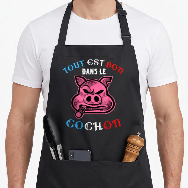 Tablier de cuisine noir avec illustration d'un cochon rose fumant et le texte tout est bon dans le cochon en bleu et rouge.