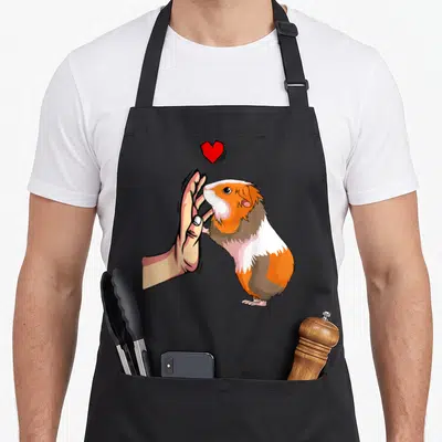 Tablier de cuisine noir avec illustration d'un cochon d'Inde tricolore touchant une main humaine sous un cœur rouge vif.