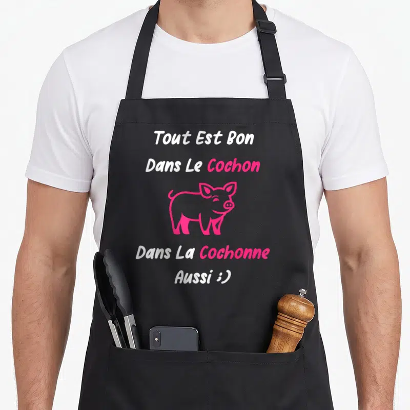 Tablier de cuisine noir avec inscription blanche et rose et illustration d'un porc souriant.