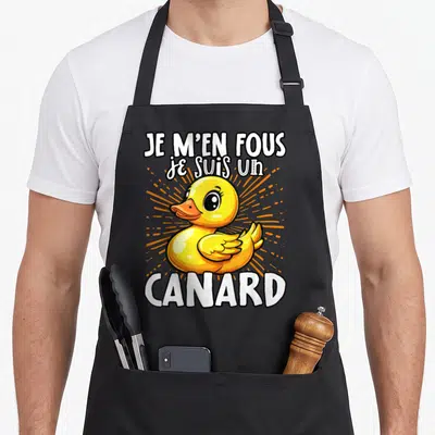 Tablier de cuisine noir avec illustration d'un canard jaune et texte blanc Je m'en fous je suis un canard sur fond orange rayonnant.