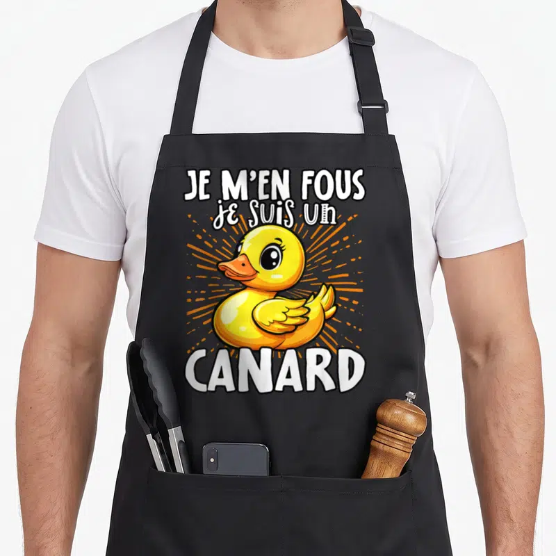 Tablier de cuisine noir avec illustration d'un canard jaune et texte blanc Je m'en fous je suis un canard sur fond orange rayonnant.