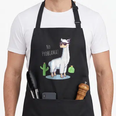Tablier de cuisine noir avec illustration d'un lama portant des lunettes de soleil et le texte No Problama entre deux cactus.