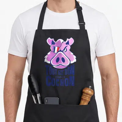 Tablier de cuisine noir avec tête de porc rose stylisée et l'inscription Tout est bon dans le cochon en lettres bleues.