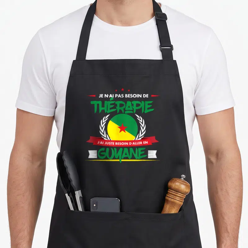 Tablier de cuisine noir avec le texte Je n'ai pas besoin de thérapie J'ai juste besoin d'aller en Guyane et un drapeau circulaire.