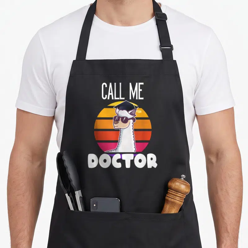 Tablier de cuisine noir avec illustration d'un lama alpaga portant une toque de docteur et des lunettes de soleil sur fond coloré.