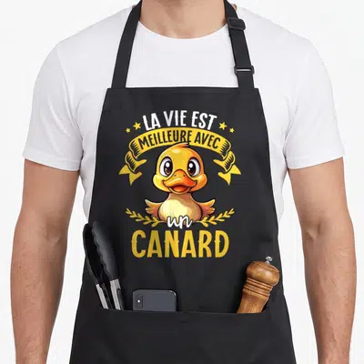 Tablier de cuisine noir avec un canard jaune souriant et le texte La vie est meilleure avec un canard entouré d'étoiles et de rubans.