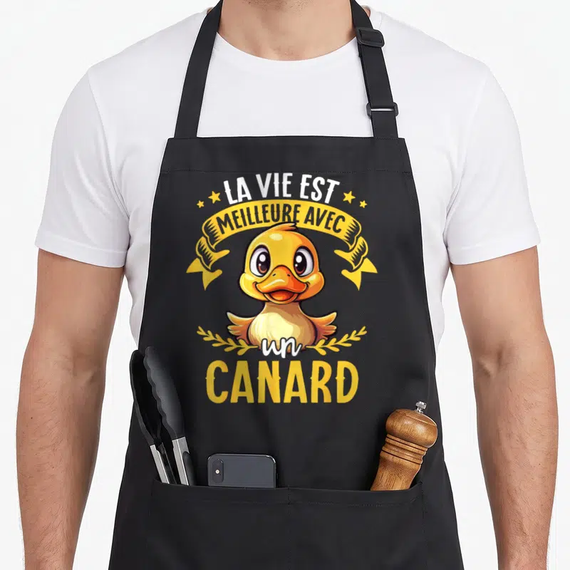 Tablier de cuisine noir avec un canard jaune souriant et le texte La vie est meilleure avec un canard entouré d'étoiles et de rubans.