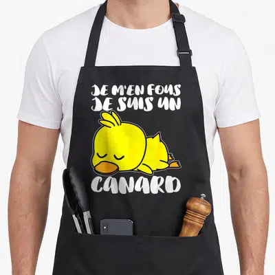 Tablier de cuisine noir avec un canard jaune dormant et l'inscription Je m'en fous je suis un canard en lettres blanches.