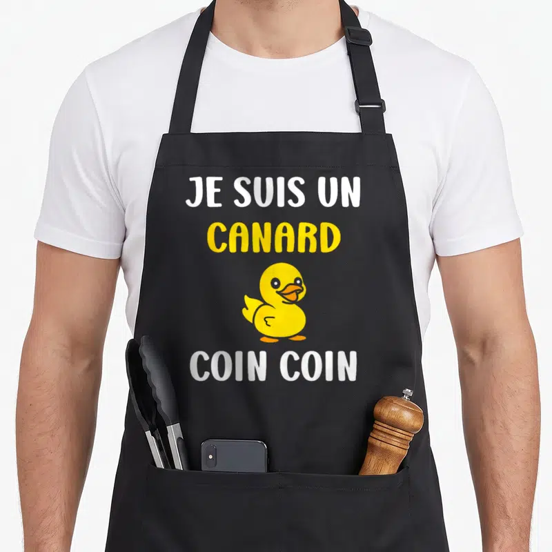 Tablier de cuisine noir avec l'illustration d'un petit canard jaune et le texte Je suis un canard Coin coin en lettres blanches et jaunes.