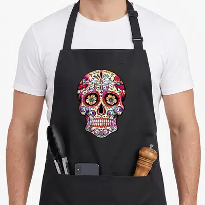 Tablier de cuisine noir avec un crâne de sucre Dia De Muertos multicolore orné de fleurs et de volutes.