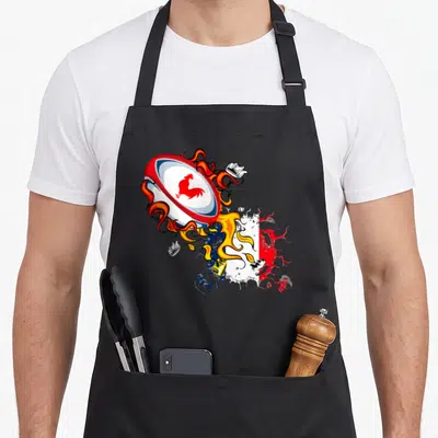 Tablier de cuisine noir avec illustration d'un ballon de rugby flamboyant portant un coq rouge et des éclats tricolores.