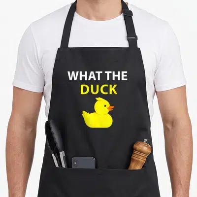 Tablier de cuisine noir avec illustration d'un petit canard jaune et le texte What the Duck en lettres blanches et jaunes.