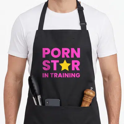 Tablier de cuisine noir avec inscription rose vif Porn Star In Training et étoile jaune centrale.