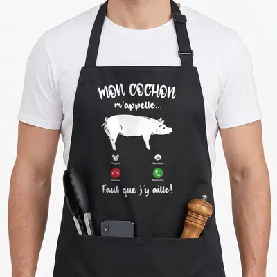Tablier de cuisine noir avec illustration blanche d'un porc et texte humoristique sur les appels téléphoniques.