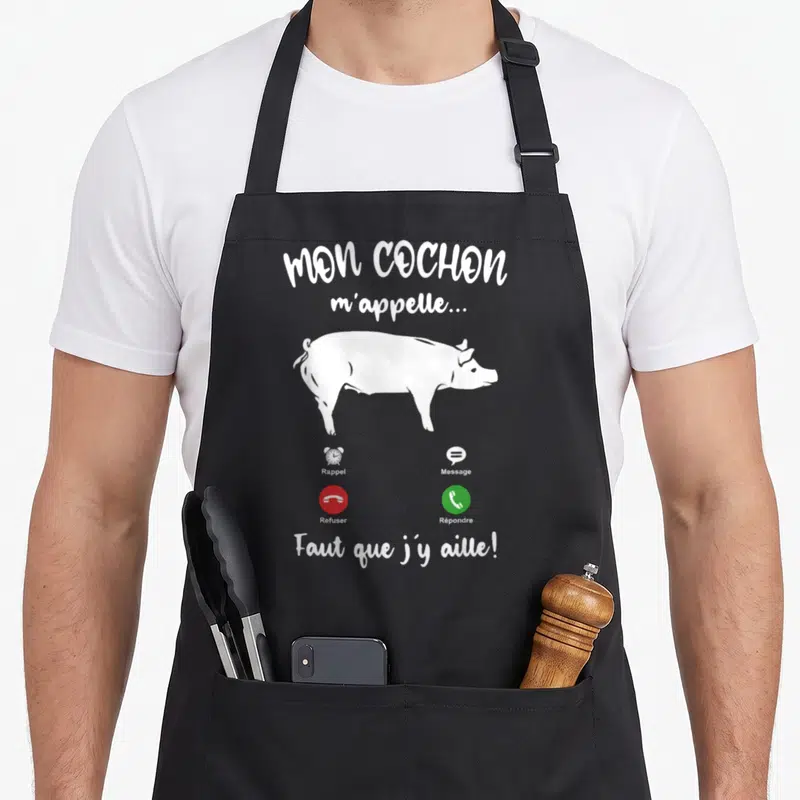 Tablier de cuisine noir avec illustration blanche d'un porc et texte humoristique sur les appels téléphoniques.
