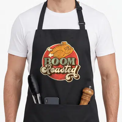Tablier de cuisine noir avec illustration d'un poulet rôti et texte Boom Roasted en style vintage sur fond rouge.