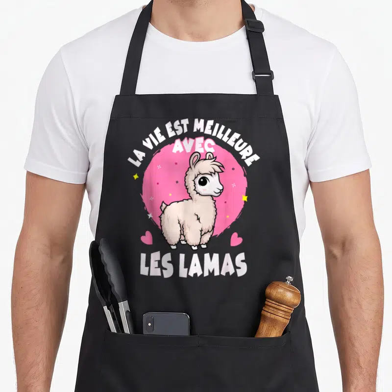 Tablier de cuisine noir avec illustration d'un lama blanc souriant sur un cercle rose et des étoiles jaunes.