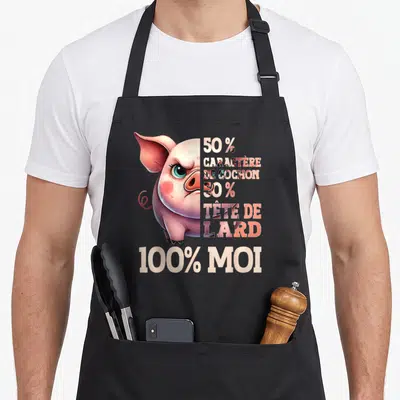 Tablier de cuisine noir avec illustration d'un porc rose aux yeux bleus et texte humoristique en blanc et rose.