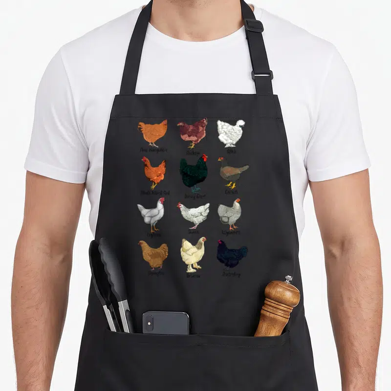 Tablier de cuisine noir avec douze illustrations colorées de poules de race et leurs noms sous chaque dessin.