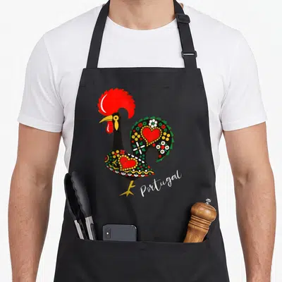 Tablier de cuisine noir avec illustration colorée d'un coq portugais Galo de Barcelos orné de cœurs et de motifs floraux verts et jaunes.