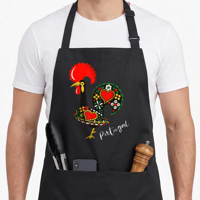 Tablier de cuisine noir avec illustration colorée d'un coq portugais Galo de Barcelos orné de cœurs et de motifs floraux verts et jaunes.
