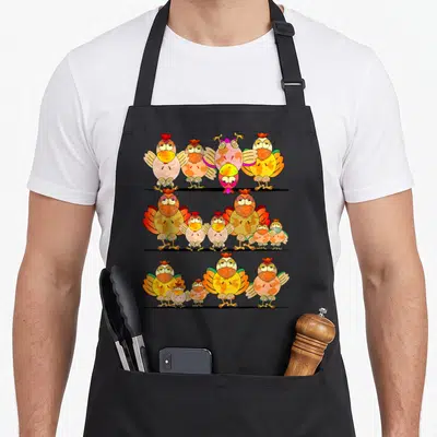 Tablier de cuisine noir avec illustration de trois rangées de poulets et poules colorés aux expressions humoristiques.