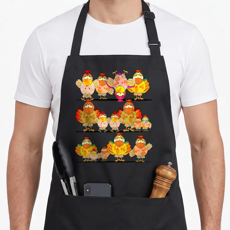 Tablier de cuisine noir avec illustration de trois rangées de poulets et poules colorés aux expressions humoristiques.
