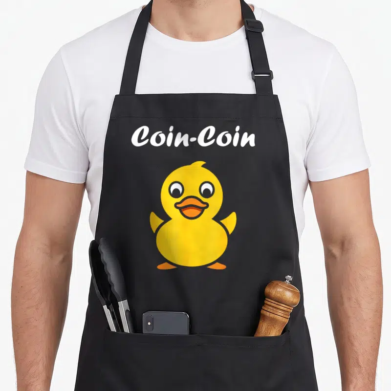 Tablier de cuisine noir avec un dessin de canard jaune et le texte blanc Coin-Coin au-dessus.