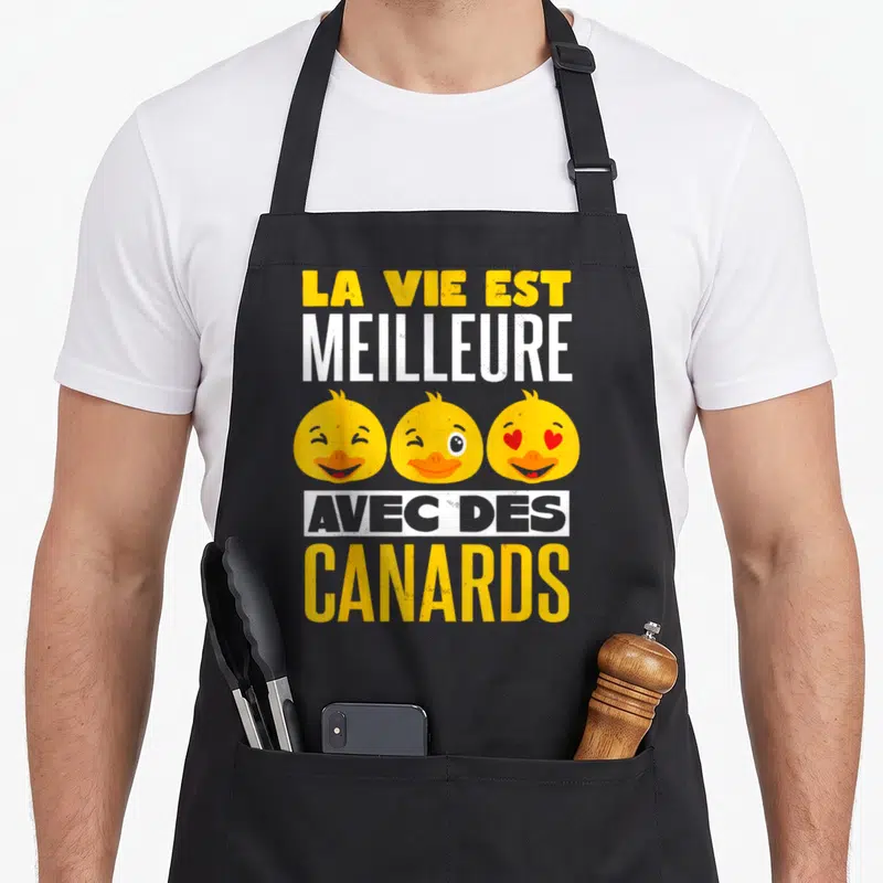 Tablier de cuisine noir avec trois têtes de canards jaunes souriants et l'inscription La Vie Est Meilleure Avec Des Canards.