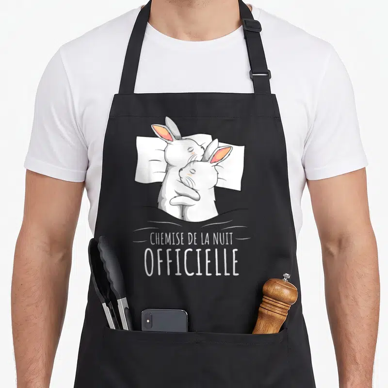 Tablier de cuisine noir avec illustration de deux lapins blancs s'enlaçant sur un oreiller et le texte « chemise de la nuit ».