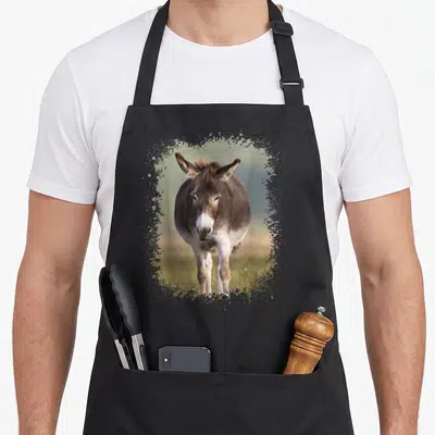 Tablier de cuisine noir avec illustration d'un âne brun à museau blanc, encadré par des éclaboussures artistiques vertes et ocre.
