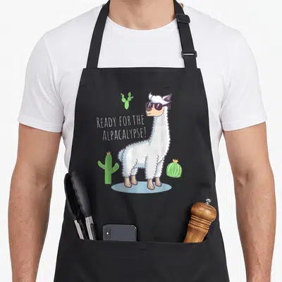 Tablier de cuisine noir avec illustration d'un alpaga en lunettes de soleil entouré de cactus verts et du texte Ready « for the » Alpacalypse.